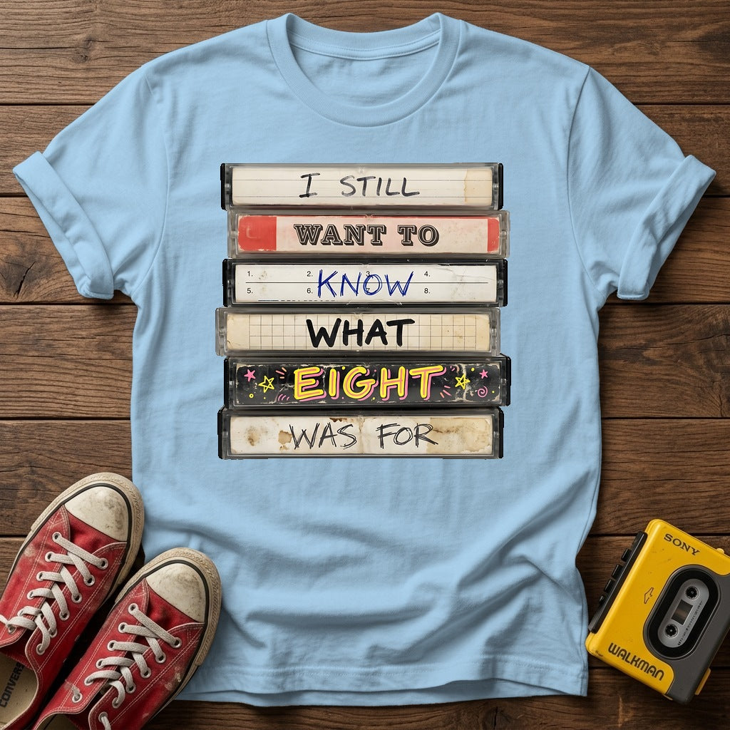 “I Still Want To Know What Eight Was For” Retro VHS Stack T Shirt — Light Blue wood flat-lay