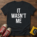 It Wasn't Me T-Shirt — Black wood flat-lay